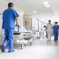 male-nurse-pushing-stretcher-gurney-bed-in-hospital-corridor-with-doctors-senior-female-patient-640x427 (1)